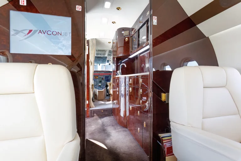 View towards the cockpit in a private jet featuring an entertainment screen with the Avcon Jet logo, highlighting the luxurious in-flight entertainment options available for a tailored flight experience.