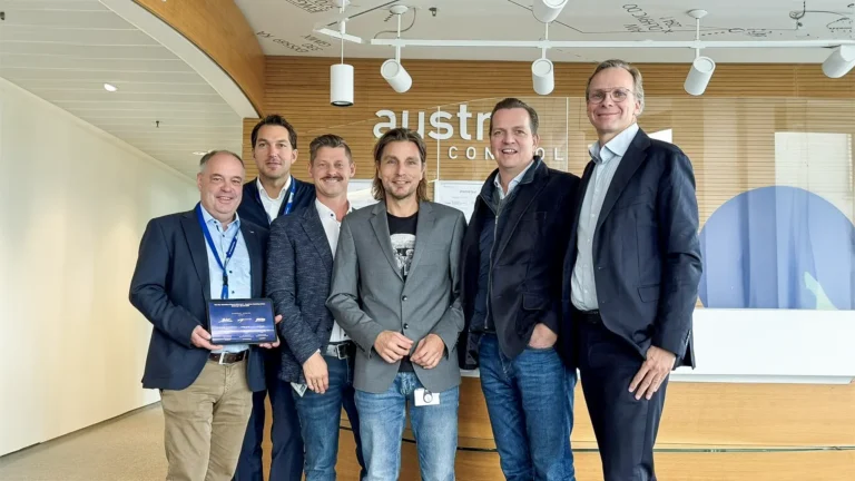 The image features six men, three from Austro Control and three from Avcon Jet, standing together at Austro Control. One person is holding an award, signifying the recognition of the "One Ops Approval".